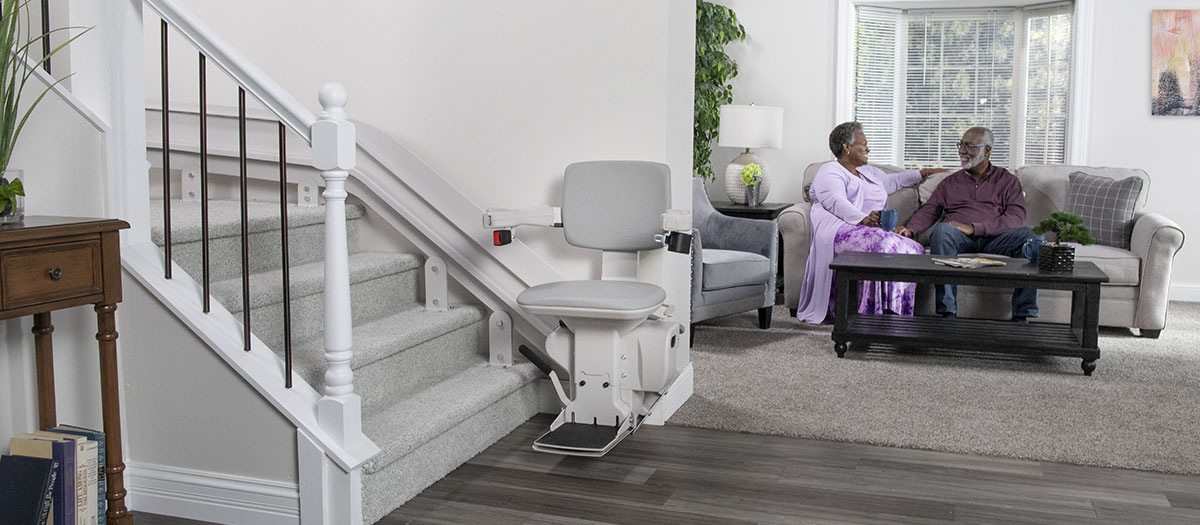 Stair lift at the bottom of a staircase with owners in living room