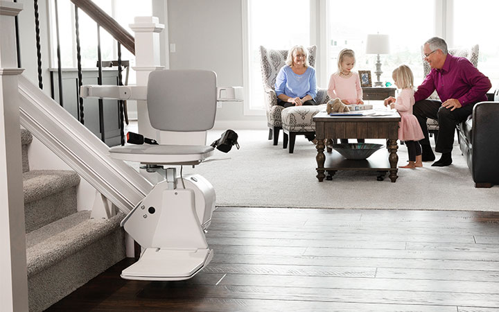 Bruno stair lift at bottom of staircase next to living room with people in the background