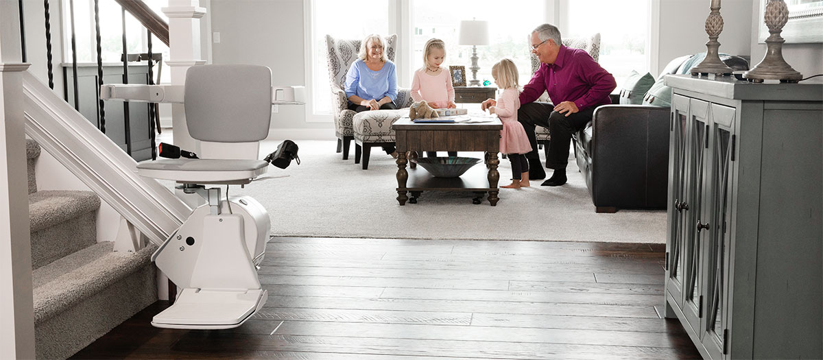 Bruno stairlift at bottom of staircase next to living room with people