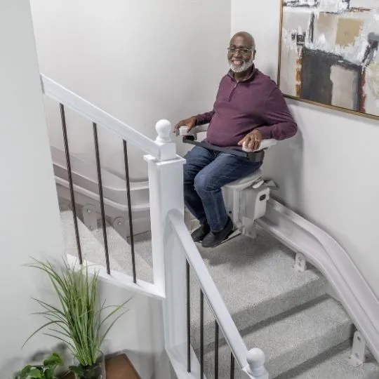 man riding a curved stairlift on steps with gray carpeting