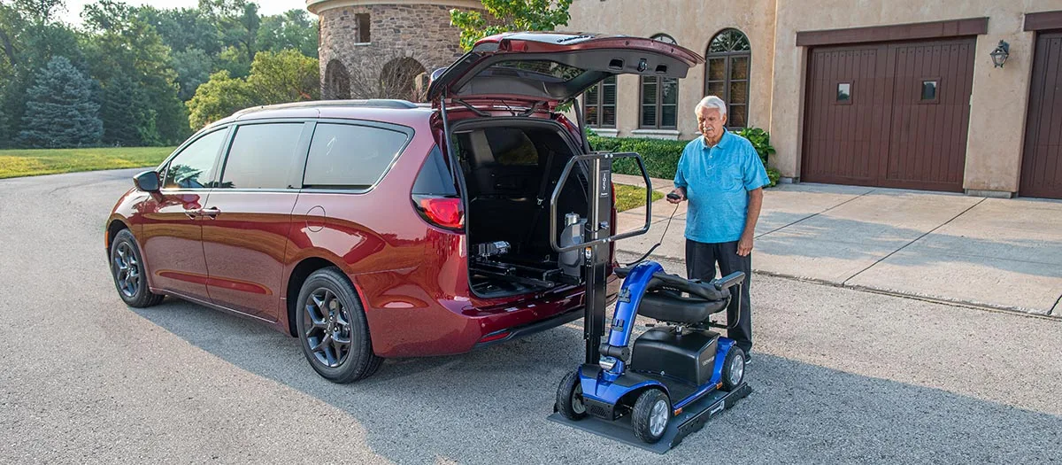 Bruno scooter lift on the back of an SUV next to a mobility device user