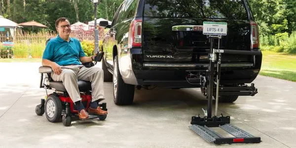a man driving a scooter onto a scooter lift that is attached to a black suv