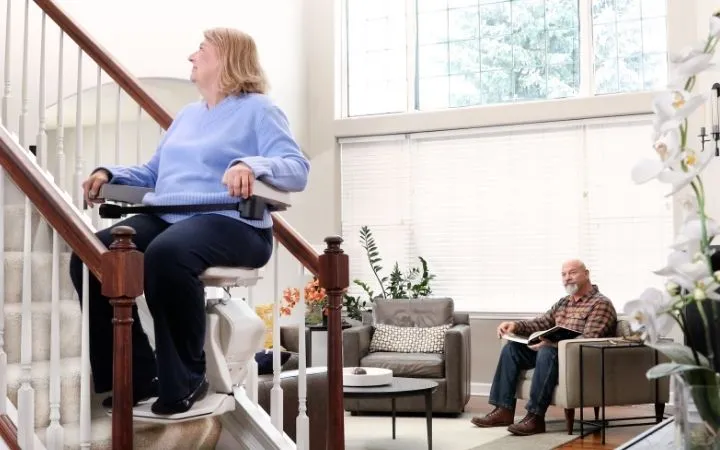 a woman riding an indoor stair lift with kids sitting on the steps watching
