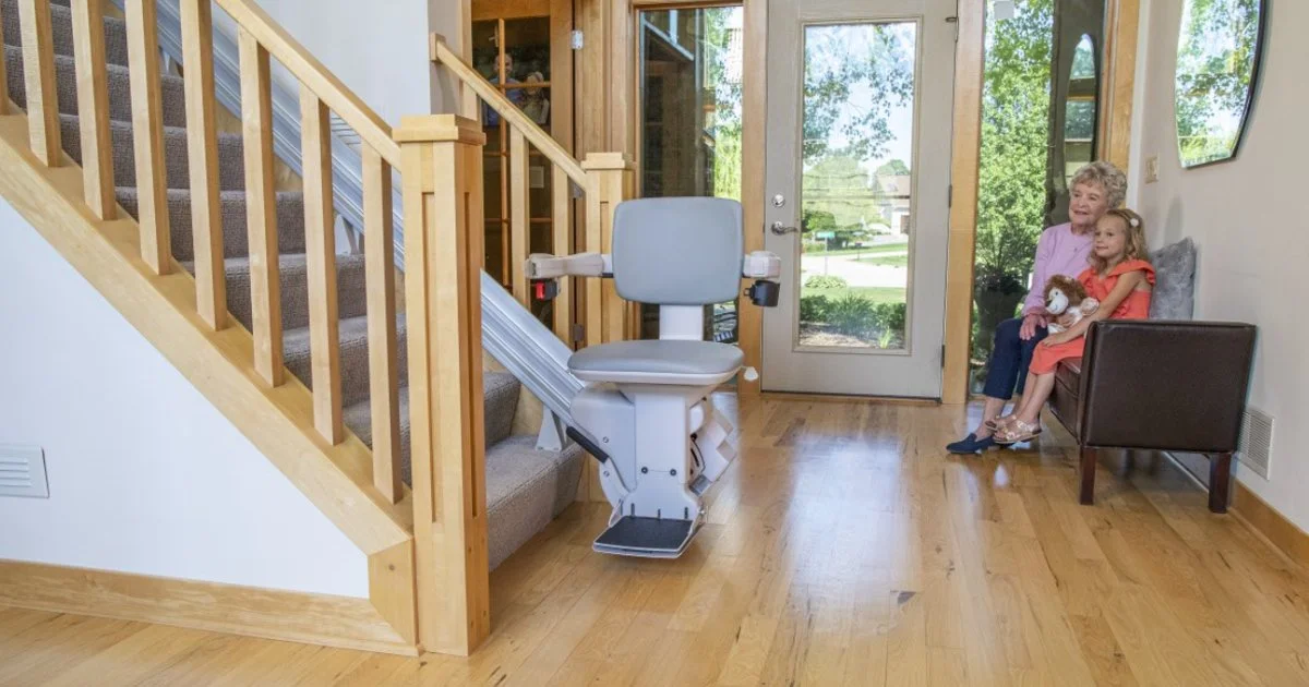 Sacramento straight rail indoor stairlift: grandmother and grandchild seated on entryway bench beside a straight indoor stair chair lift