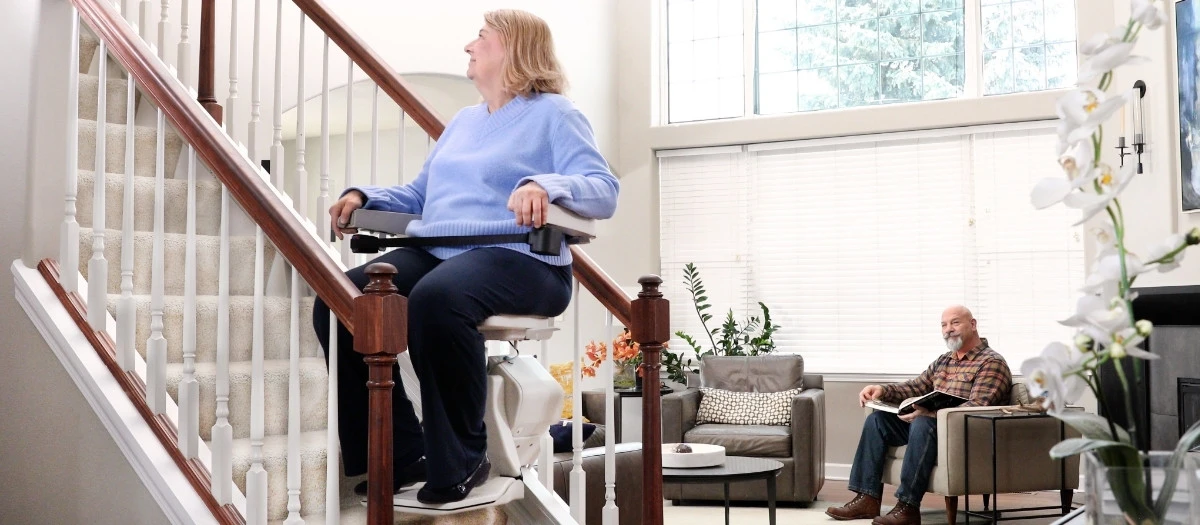 a woman riding an indoor stair lift with kids sitting on the steps watching