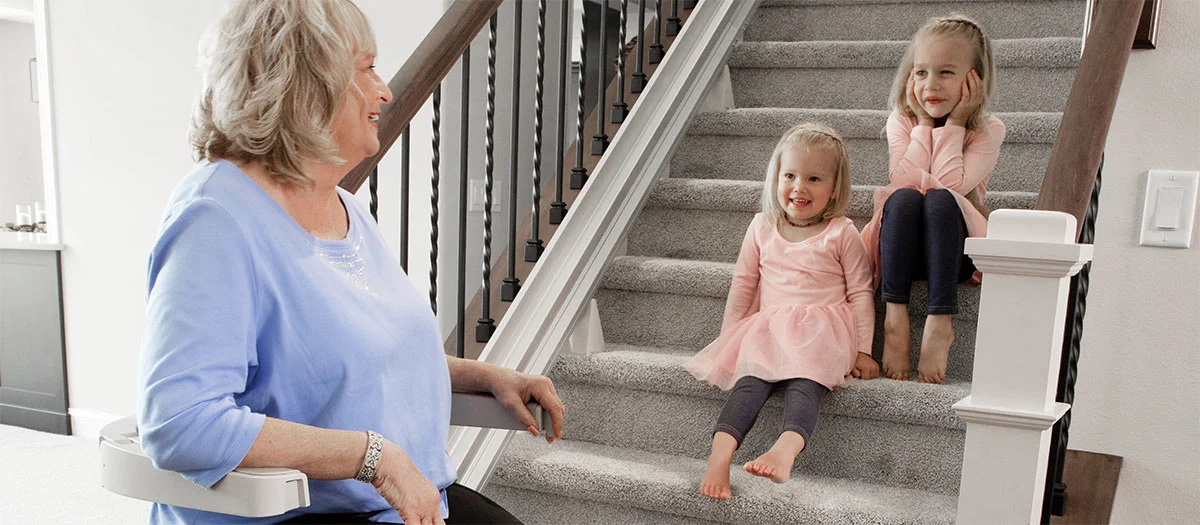 a woman riding an indoor stair lift with kids sitting on the steps watching